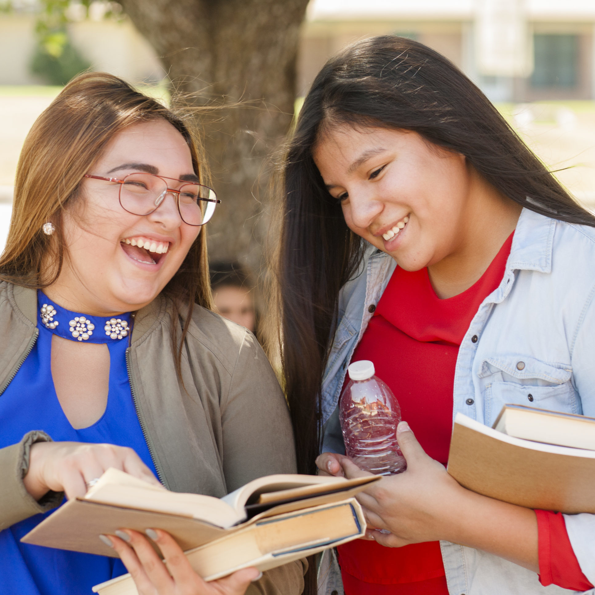 Two young teen girls stand together outside of school building laughing