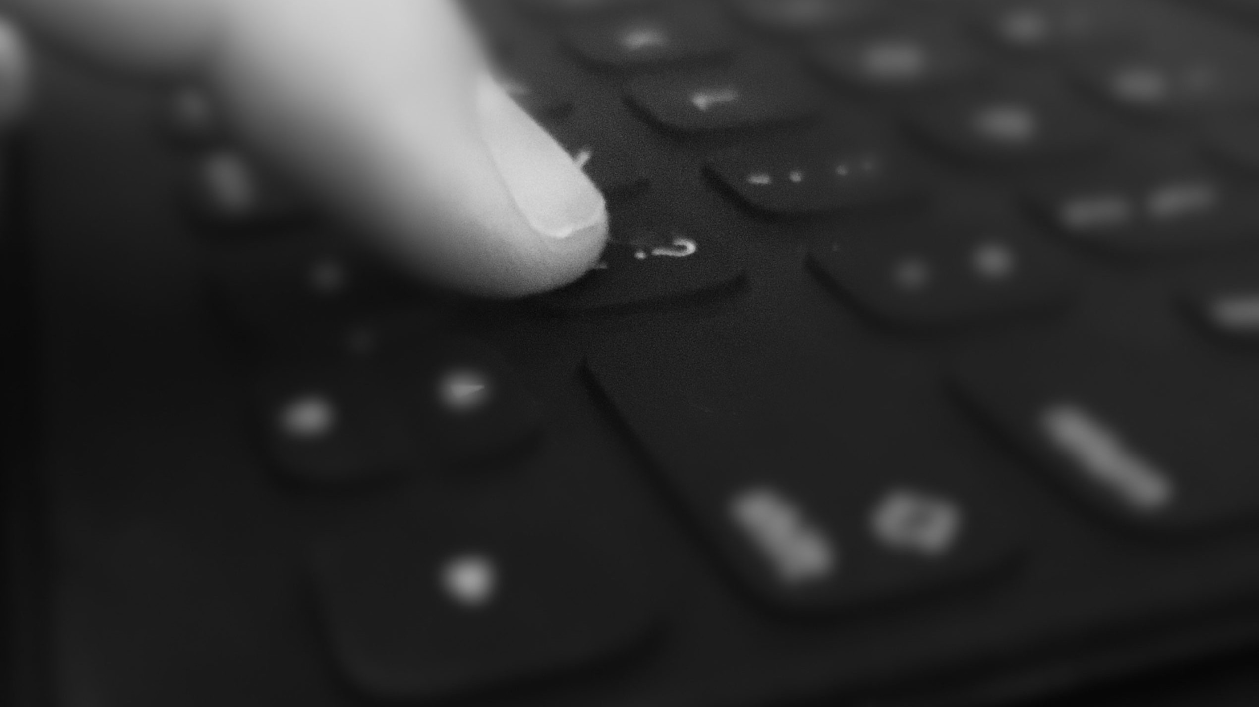A pointer finger touches the question mark key on a keyboard. Black and white filter shades photo.