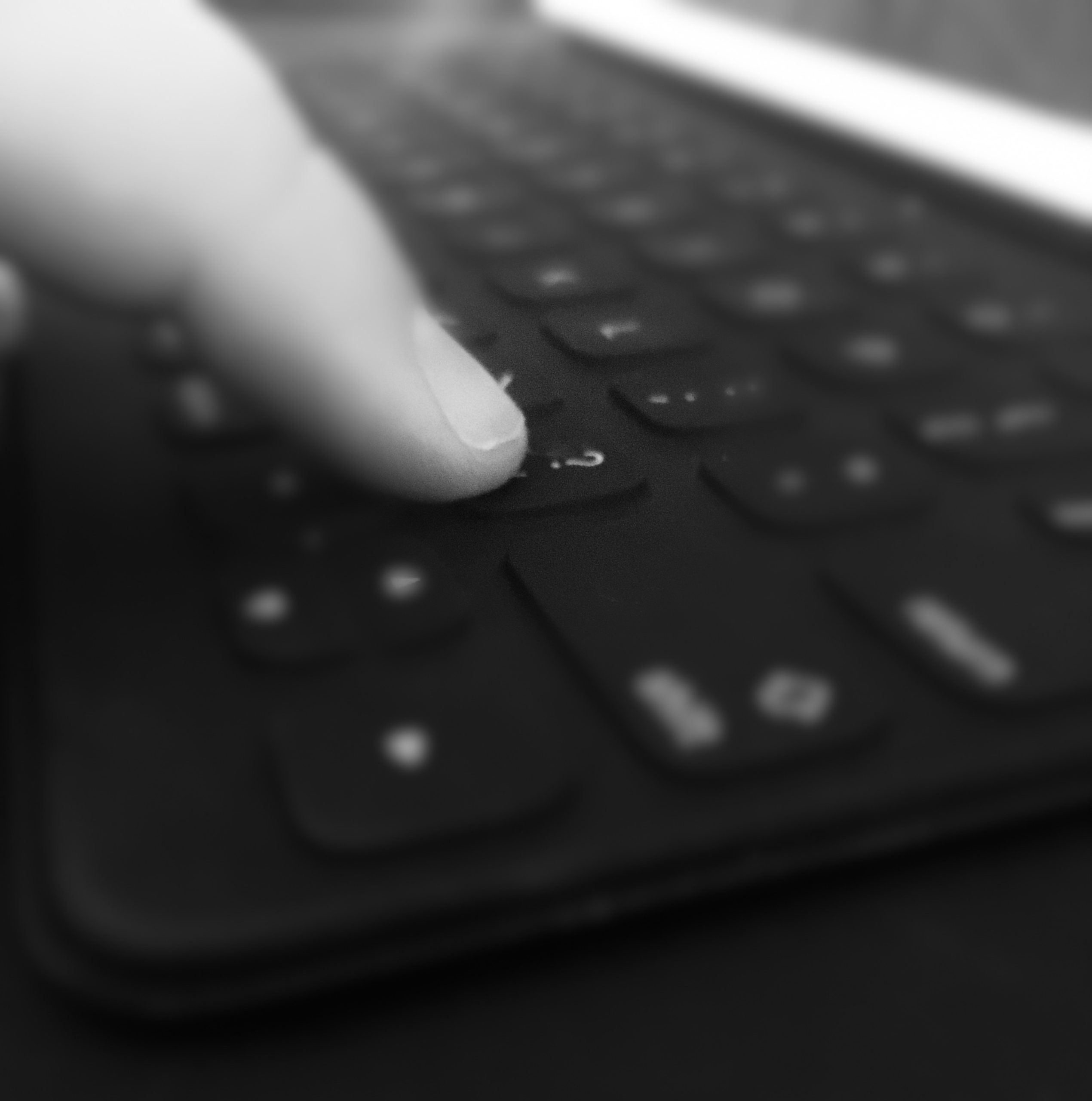 A pointer finger touches the question mark key on a keyboard. Black and white filter shades photo.