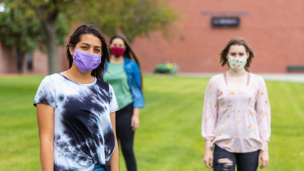 A group of Colorado teen girls stand masked and distanced in an open field.